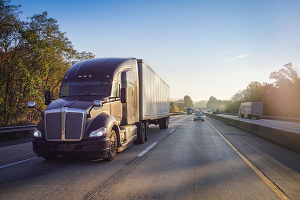 Large semi-truck driving down the highway with other vehicles in the distance.