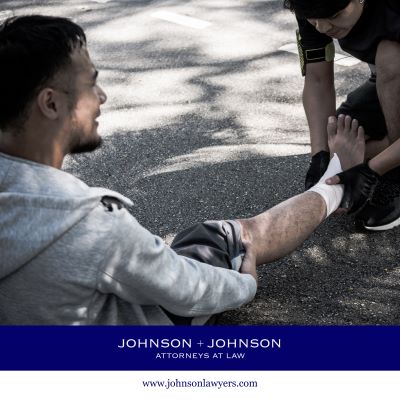 Injured man sitting on the road while another person helps bandage his leg.