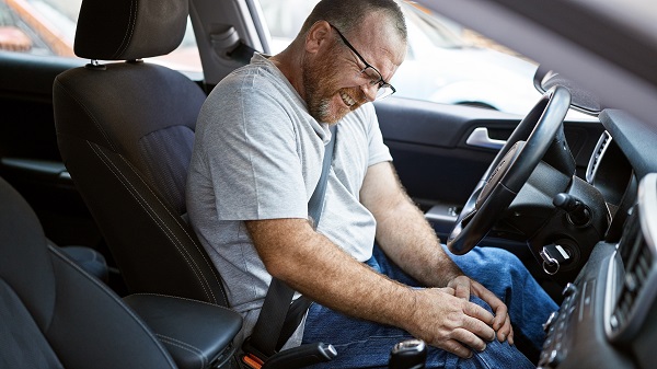 Male driver holds knee in pain after getting into a car accident.