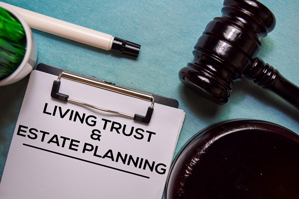 A dark wooden gavel rests next to a clipboard with a document titled "LIVING TRUST & ESTATE PLANNING."