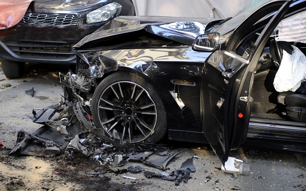 Two heavily damaged black cars. The airbags are deployed and there is crash debris in the road.