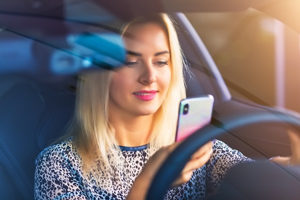 Young smiling woman driver using a smartphone in a modern luxury car to indicate she is texting and driving.